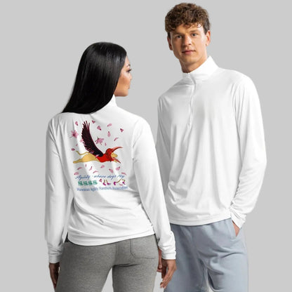 
A man and a woman modeling athletic apparel in a studio setting. The woman is shown from the back wearing a white long-sleeve quarter-zip top with a dog masked and winged as a colorful bird graphic and the words 'Agility, where dogs fly' on the back, paired with gray jogger pants.